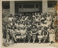 Photo of women between palmetto trees in front of brick building