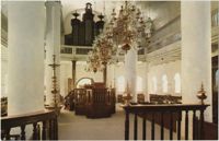 Interior of Mikve Israel-Emanuel Synagogue, dedicated in 1732, oldest in continuous use in Western Hemisphere. View is towards main entrance, showing Tebah (reading platform) and beautiful old brass chandeliers over sandcovered floor flanked by mahogany wooden benches.