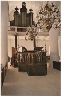 View of interior of Mikve Israel-Emanuel Synagogue looking towards main entrance and Tebah (reading platform) in center and showing beautiful brass chandeliers over two centuries old. Benches are on both sides of sand-covered floor.