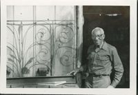 Photograph Philip Simmons standing next to railing outside his workshop.