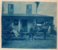 Man and woman in horse buggy in front of 2 story house