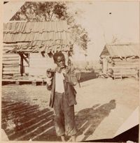 Boy with wooden flute in front of outbuildings